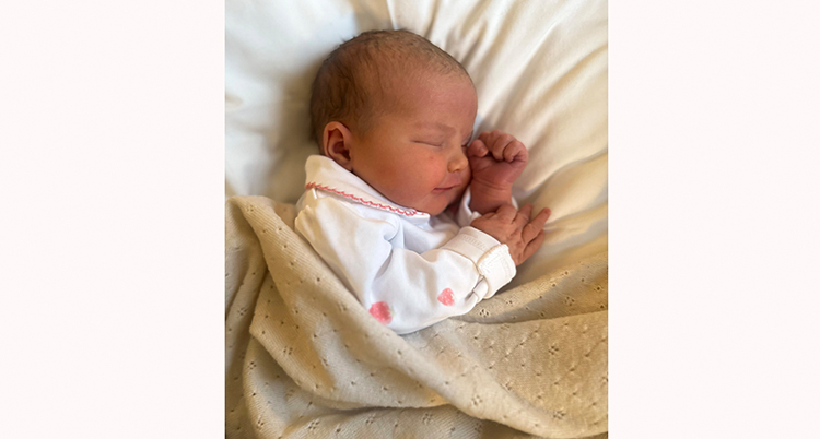 En baby i vit tröja ligger under en beige filt.