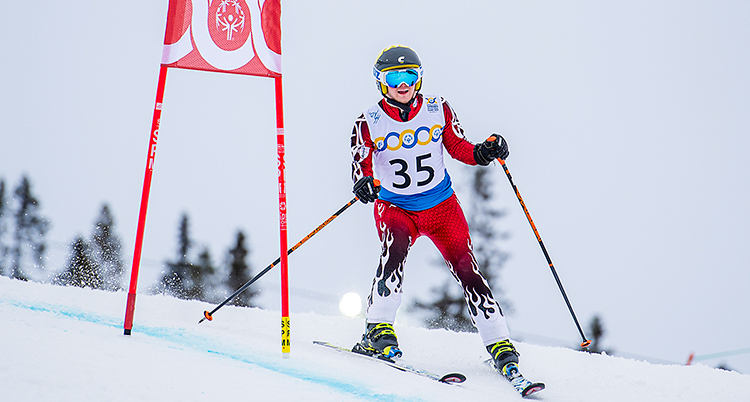 Han har en röd dräkt och hjälm. Han åker slalom i en backe.