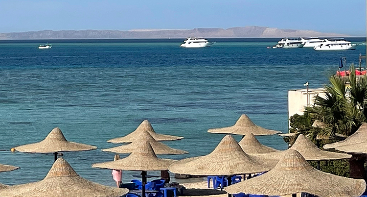 Båtar på ett hav. Strand med parasoller i förgrunden.