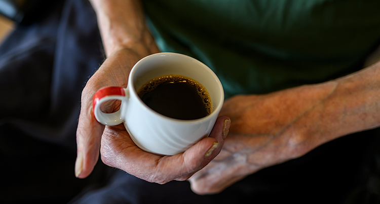 En gammal person håller en kopp med kaffe.